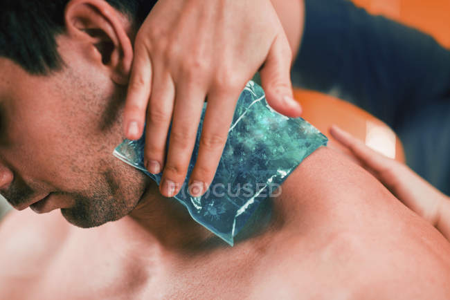 Terapeuta femenina aplicando compresa de hielo en el doloroso cuello del atleta masculino
. - foto de stock