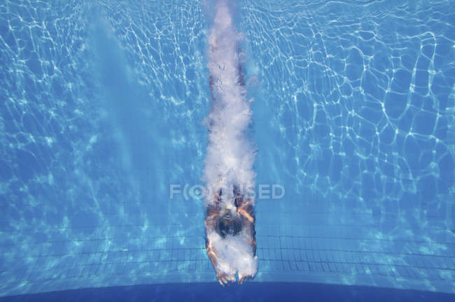 Female diver swimming with splashes underwater after athletic jump in pool. — Stock Photo