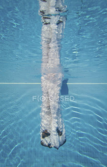 Mergulhador masculino nadando com salpicos subaquáticos após salto atlético na piscina . — Fotografia de Stock