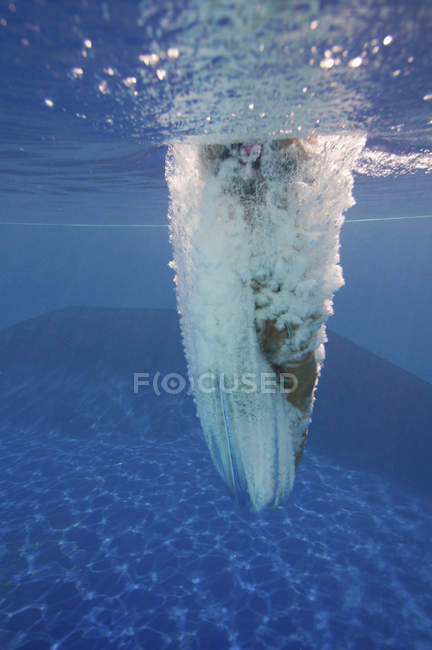Female diver swimming with splashes underwater after athletic jump in pool. — Stock Photo