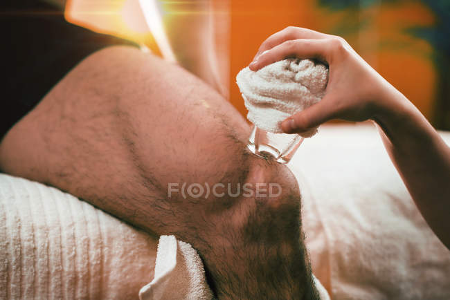 Gros plan du physiothérapeute féminine effectuant un massage cryogénique pour soulager la douleur au genou . — Photo de stock