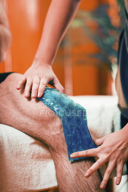 Mains de thérapeute féminine mettant la banquise sur le genou douloureux de l'athlète masculin . — Photo de stock