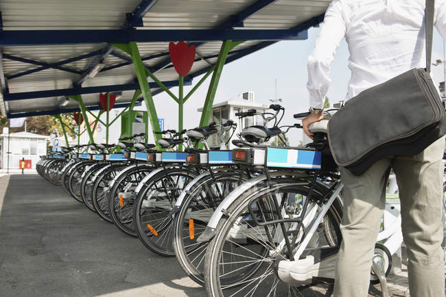 Commuter femenino tomando bicicleta eléctrica de la estación de bicicletas compartidas
. - foto de stock