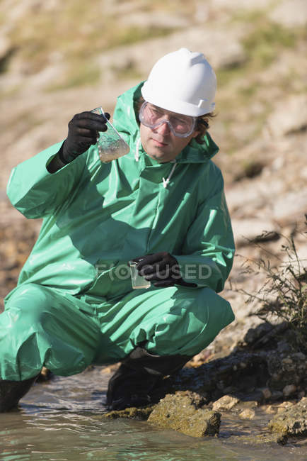 Water quality inspector filling sample container with river water at pollution site. — Stock Photo