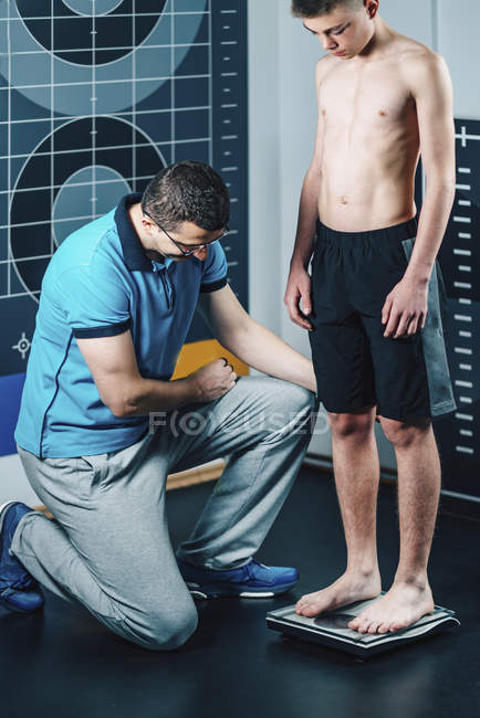 Fisioterapeuta midiendo el peso del adolescente . - foto de stock