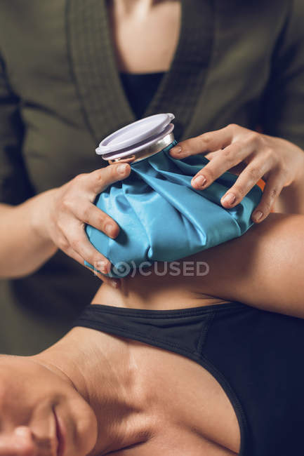 Manos de fisioterapeuta sosteniendo bolsa de hielo azul en el hombro doloroso de la deportista
. - foto de stock