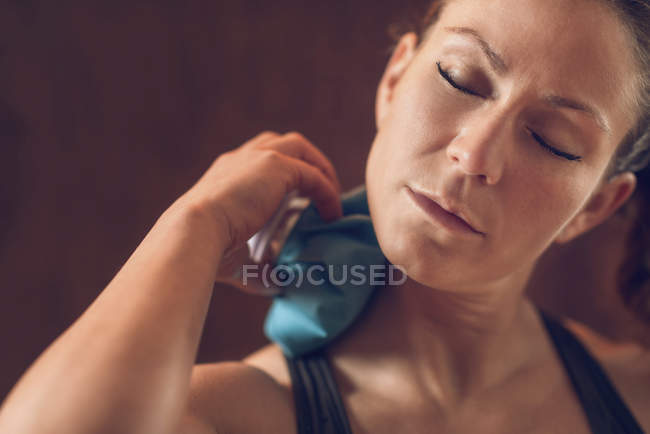 Sportswoman holding blue ice pack on painful neck. — Stock Photo
