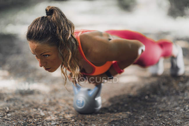Atleta feminina se exercitando em prancha com kettlebell no parque . — Fotografia de Stock