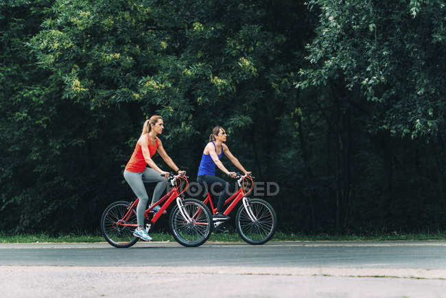 Две женщины среднего возраста вместе катаются на велосипеде в парке . — стоковое фото