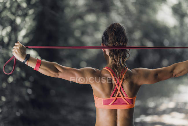 Vue arrière de l'athlète féminine faisant de l'exercice avec bande élastique dans le parc . — Photo de stock