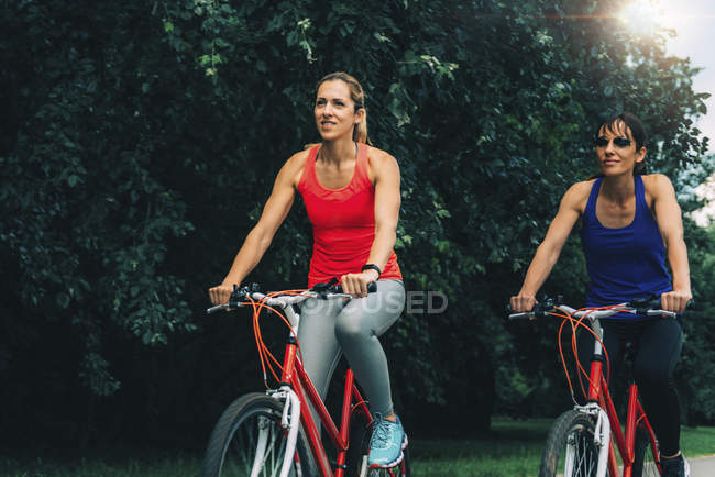 Duas mulheres adultas médias pedalando juntas no parque . — Fotografia de Stock