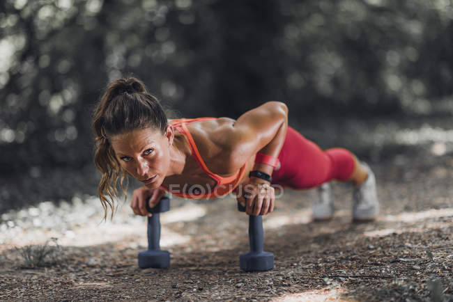 Female athlete doing push-up with dumbbells in park. — Stock Photo