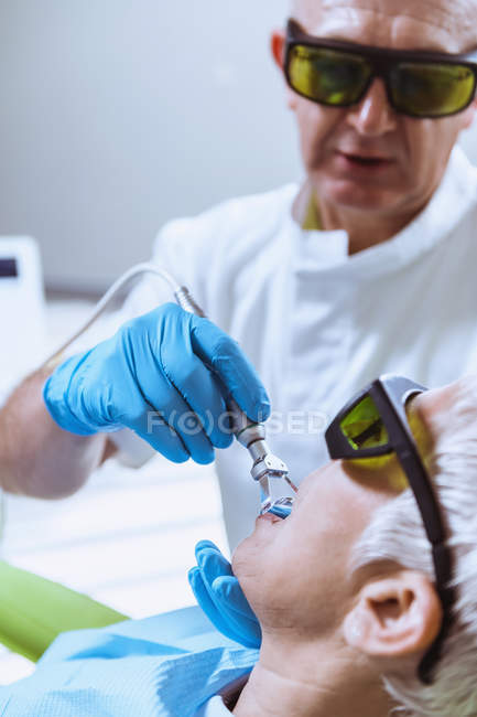 Male dentist performing laser teeth whitening at female patient at dental clinic. — Stock Photo