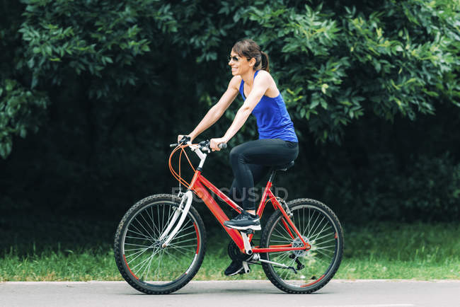 Donna sorridente mentre va in bicicletta nel parco . — Foto stock