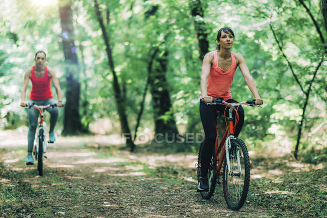 Mujer riding bikes together in sunny park . - foto de stock