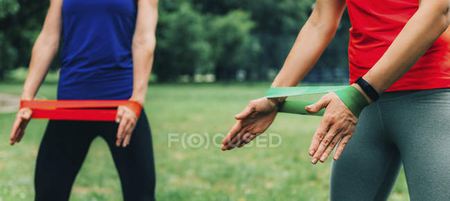 Sezione centrale di amiche che si esercitano con elastici nel parco verde . — Foto stock