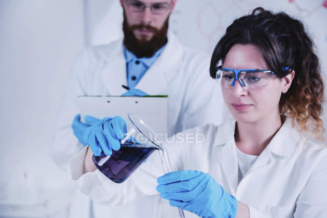Young scientists doing experiment in laboratory with liquid. — Stock Photo