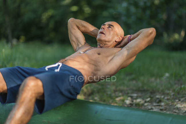 Fit senior man practicing abdominal crunches in park. — Stock Photo