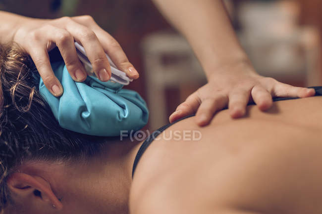 Hands of physician holding blue ice pack on painful female neck. — Stock Photo