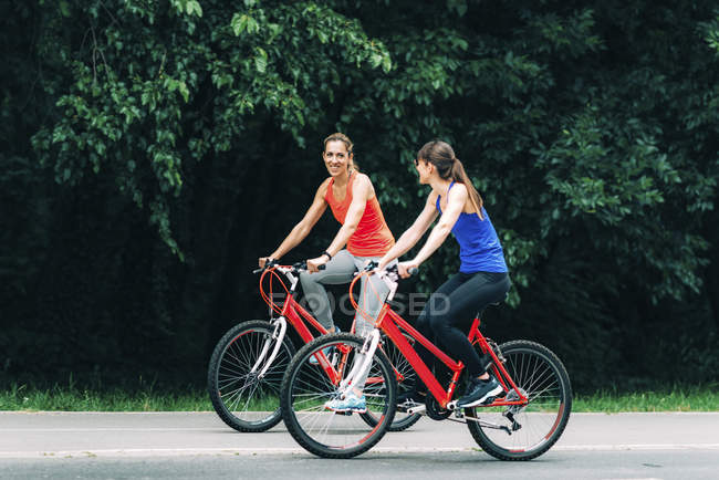 Amigas montando bicicletas juntas en el parque . - foto de stock