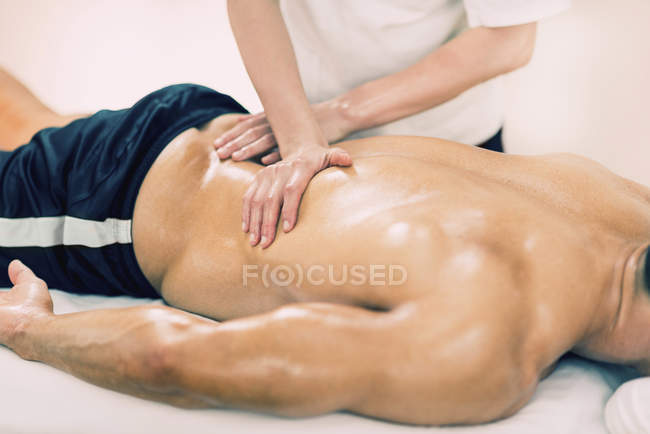 Fisioterapista massaggiando atleta maschile parte bassa della schiena . — Foto stock