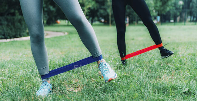 Low section of female friends exercising with elastic bands in green park. — Stock Photo