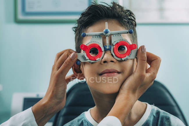 Мальчик младшего возраста в офтальмологических очках при осмотре глаз в клинике . — стоковое фото