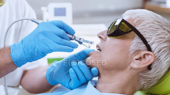 Dentista realizando blanqueamiento de dientes láser en paciente femenina en clínica dental . - foto de stock