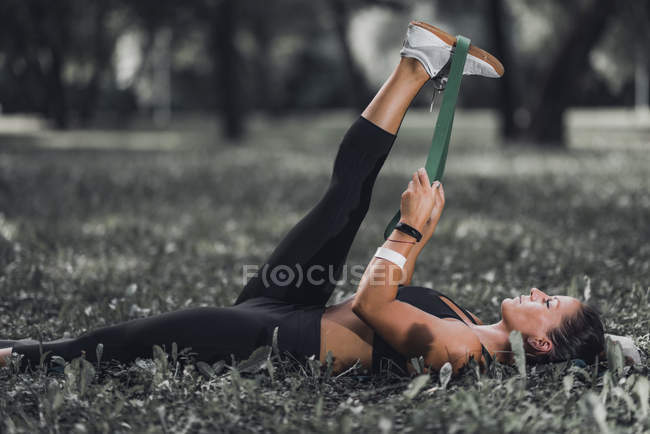 Athletic woman stretching with elastic band after exercise in park. — Stock Photo