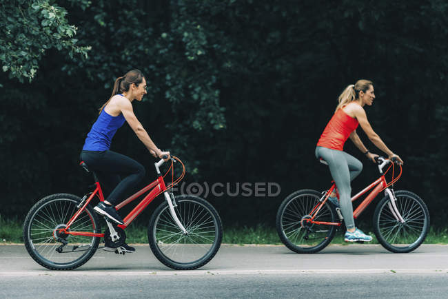 Female friends riding bikes together in park. — Stock Photo