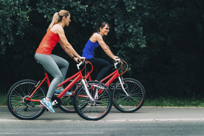 Amigos do sexo feminino andar de bicicleta juntos no parque . — Fotografia de Stock