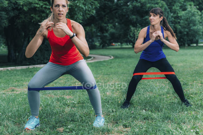 Female friends exercising with elastic bands in green park. — Stock Photo