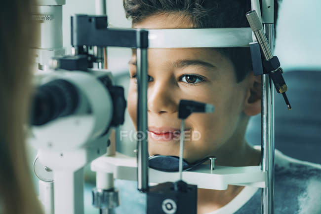Menino da idade elementar submetido a exame visual com lâmpada de fenda na clínica de oftalmologia . — Fotografia de Stock