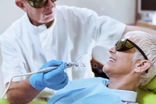 Odontólogo masculino realizando blanqueamiento de dientes láser en paciente femenino en clínica dental . - foto de stock