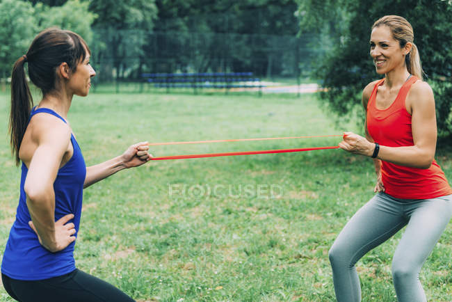 Female friends exercising with elastic band in summer park. — Stock Photo