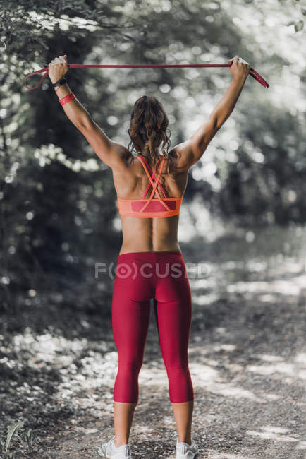Rear view of female athlete exercising with elastic band in park. — Stock Photo