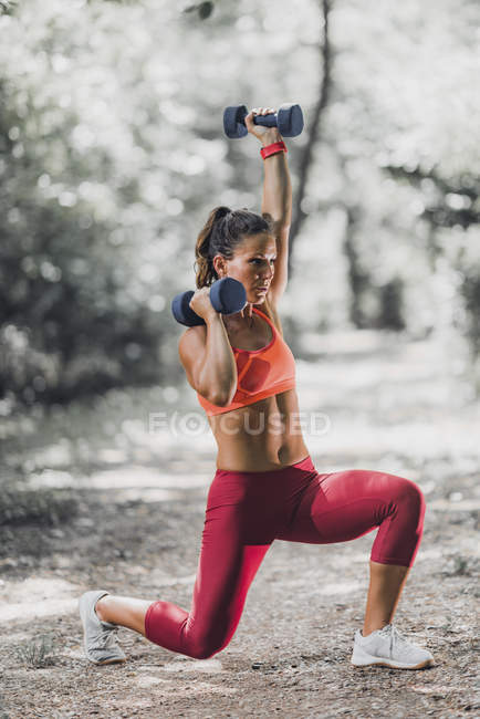 Athlète féminine faisant de l'exercice avec haltères dans le parc . — Photo de stock