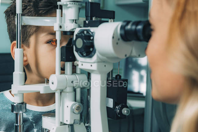 Офтальмолог вивчає очі хлопчика з лампою в клініці . — стокове фото