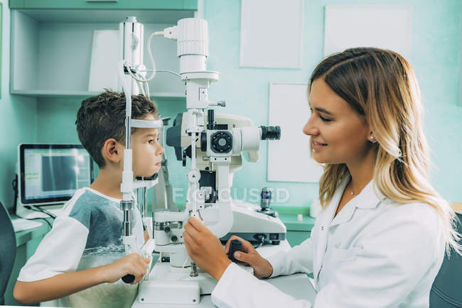 Офтальмолог вивчає очі хлопчика з лампою в клініці . — стокове фото