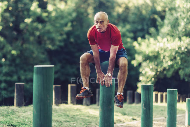 Ajuste hombre mayor ejercicio y saltar sobre postes de madera en el parque . - foto de stock