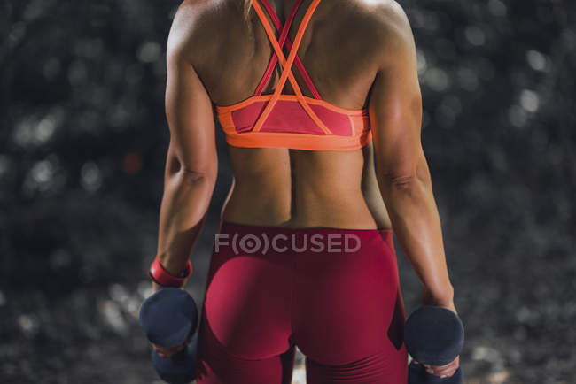 Rear view of female athlete exercising with dumbbells in park. — Stock Photo