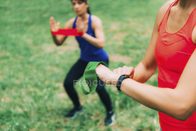 Mujer comprobando el progreso en smartwatch después de entrenar al aire libre con un amigo . - foto de stock