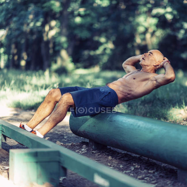 Fit senior man exercising on wooden equipment in park. — Stock Photo