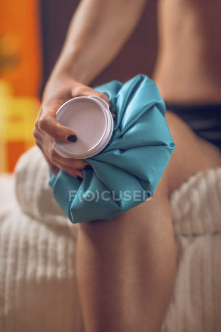 Close-up of sportswoman holding blue ice pack on painful knee. — Stock Photo