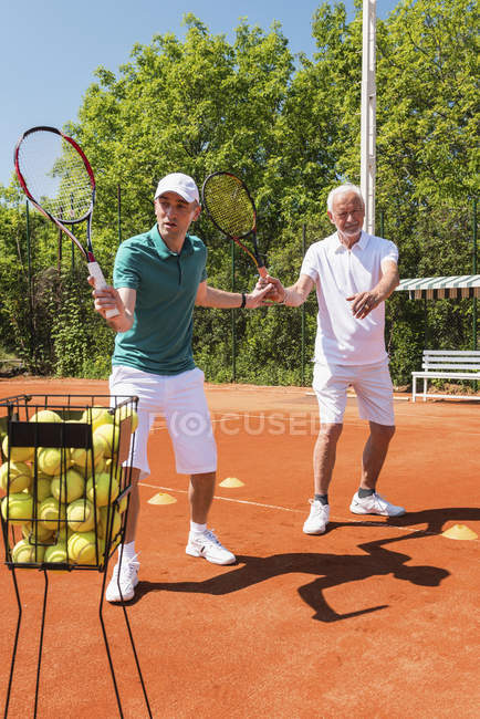 Sénior ativo praticando em aula de tênis com instrutor masculino . — Fotografia de Stock