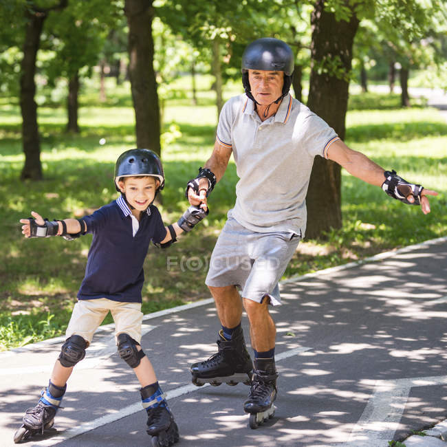 Abuelo y nieto disfrutando patinando en el parque de verano . - foto de stock