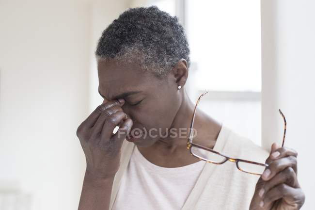 Mature woman with tension headache holding glasses. — Stock Photo