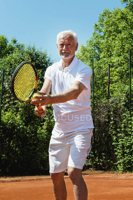Joueur de tennis senior servant la balle sur le court . — Photo de stock