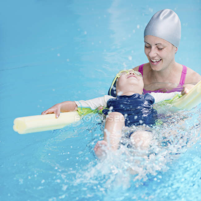 Little boy swimming on back with water noodle in swimming pool. — Stock Photo