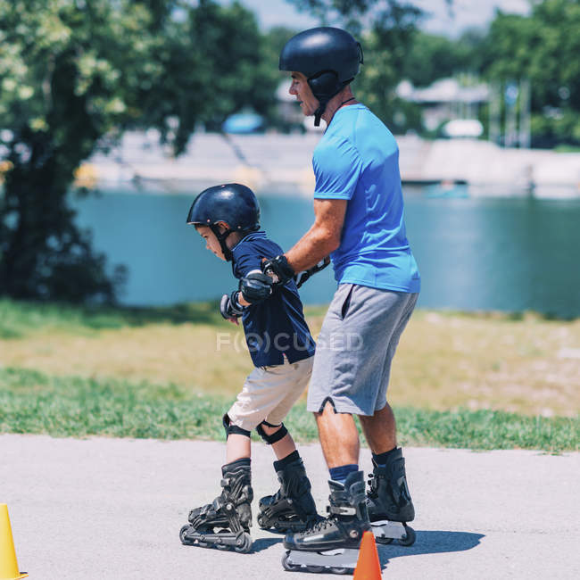 Niño aprendiendo patinaje sobre ruedas con el abuelo en la carretera con conos . - foto de stock